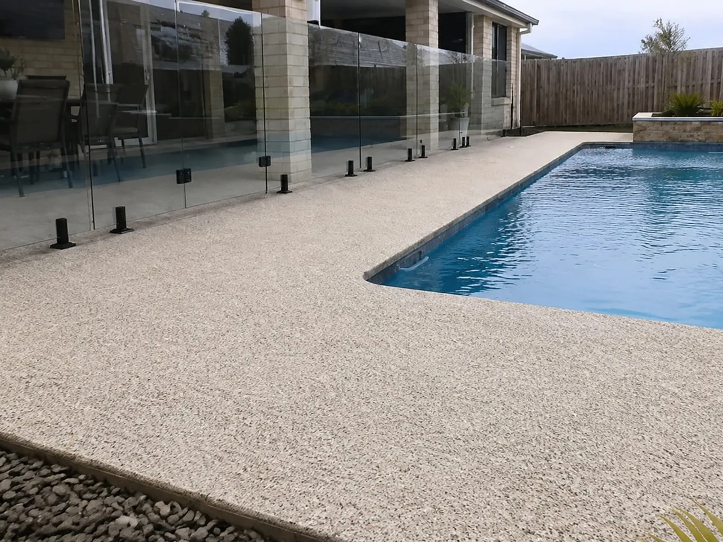 Exposed aggregate pool surround wrapping a swimming pool behind frameless glass fencing at a Toowoomba home
