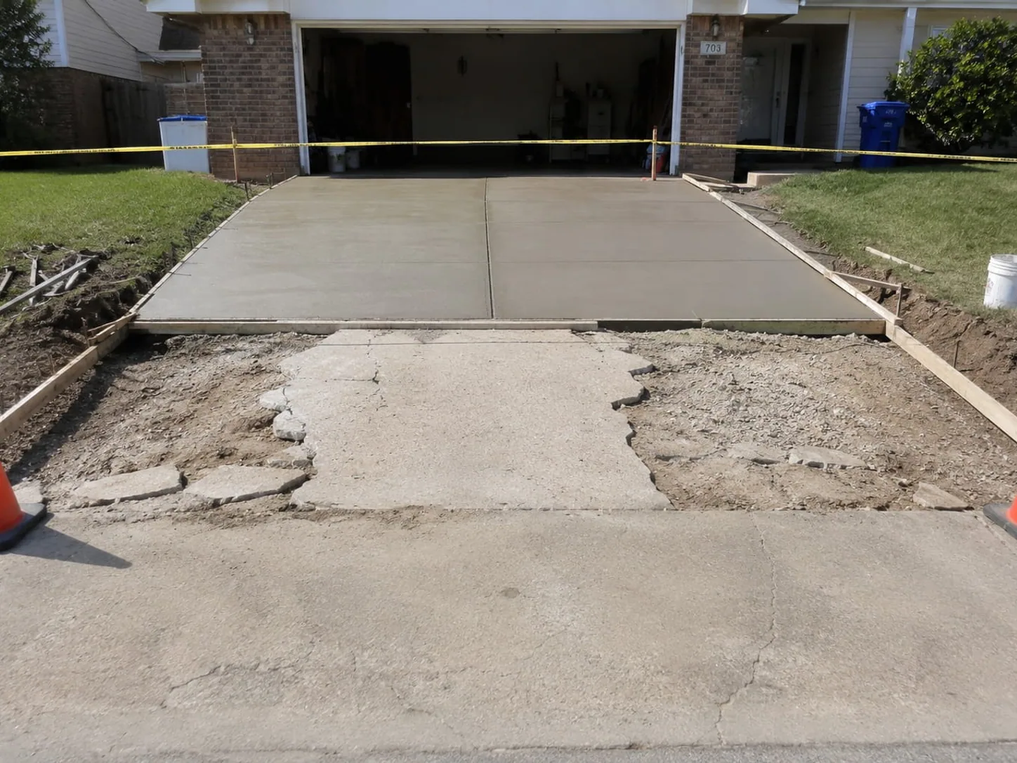 Old driveway slab broken out beside the freshly poured replacement section, taped off while it cures