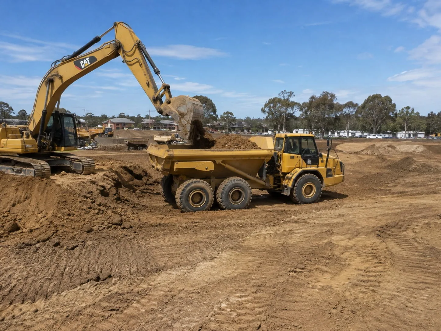 Excavator loading an articulated dump truck while shaping a building pad on a Toowoomba site