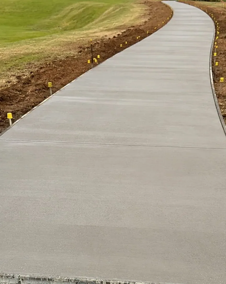 Wide concrete pathway curving away across a lawn, freshly poured with the edge pegs still in place
