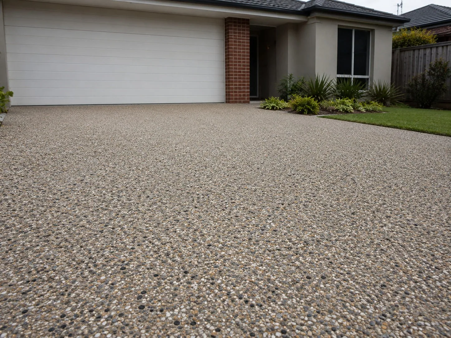 Exposed aggregate driveway in mixed river pebble running the full width of a white double garage